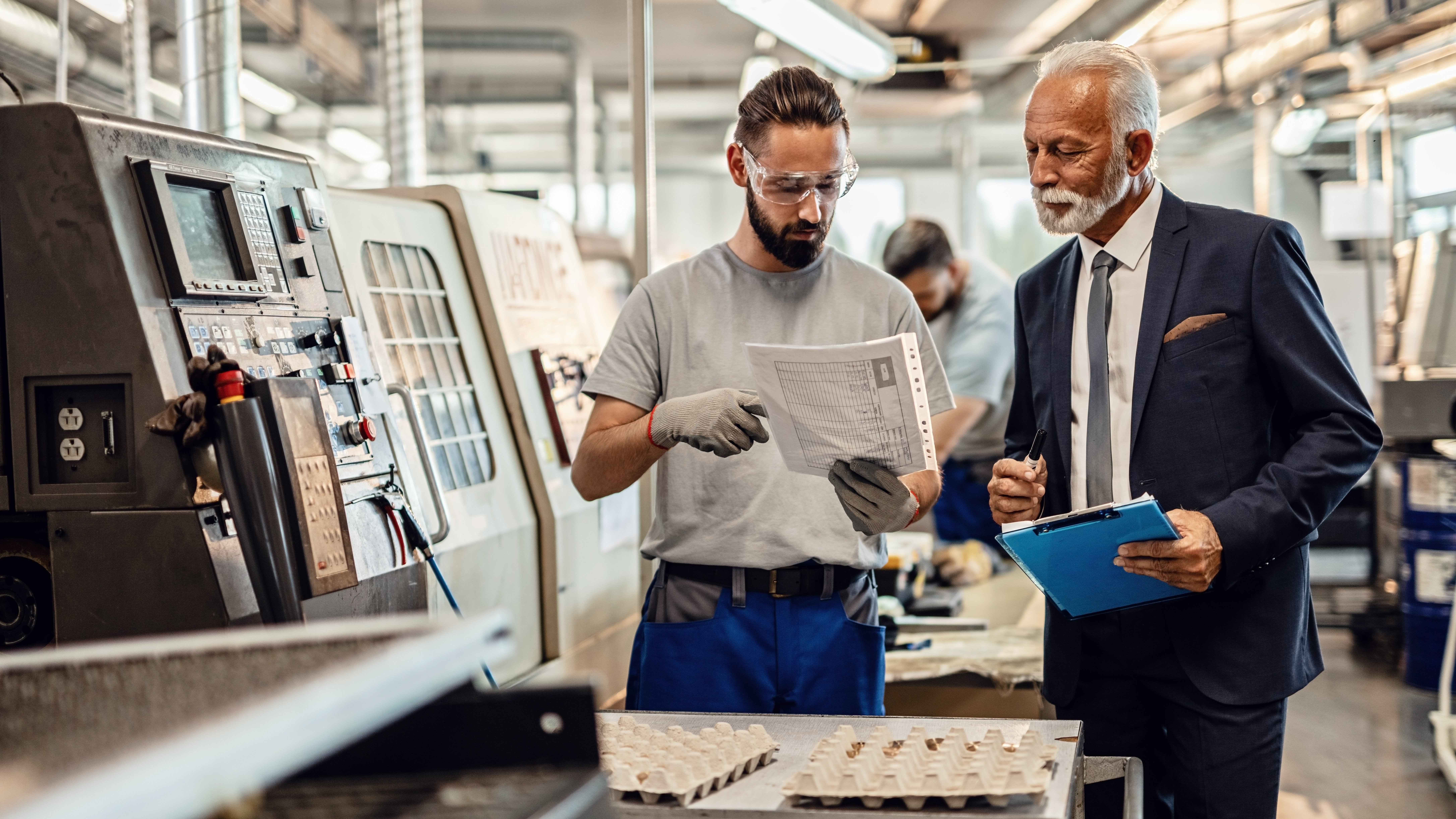 Manufacturing setting with two individuals engaged in a business discussion.
